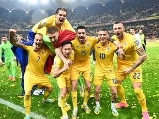 Un grup de fotbaliști în echipament galben sărbătoresc pe un teren de fotbal sub luminile unui stadion plin de spectatori.