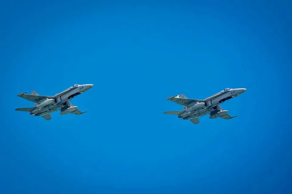 Două avioane de vânătoare gri zboară în formare pe un cer albastru intens.