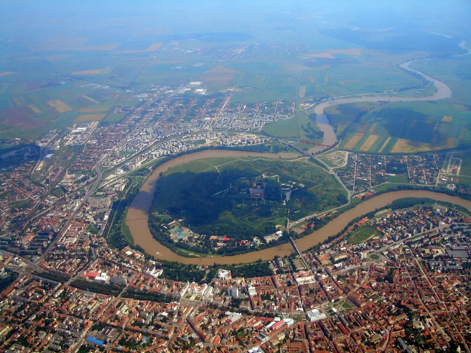 O vedere aeriană a unui oraș cu clădiri, străzi și un râu care curge prin zona urbană și câmpie.