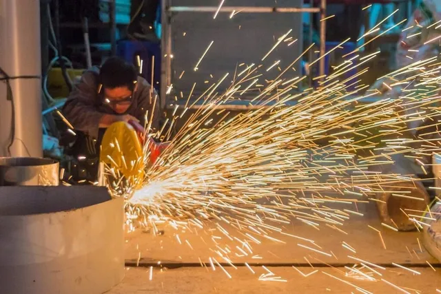 O persoană poartă ochelari de protecție și utilizează un instrument pentru tăiere, generând un nor dens de scântei strălucitoare pe un fundal de atelier.