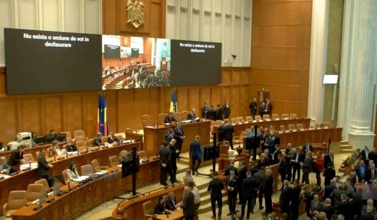 O sală de ședințe cu mese de lemn, scaune maronii și un ecran mare afișând imagini cu oameni într-un decor oficial.