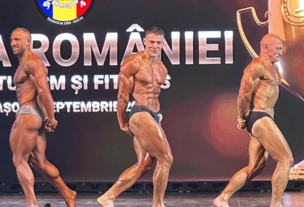 Trei bărbați musculosi în costume de competiție de culturism pozează pe o scenă în fața unui fundal negru cu text alb.