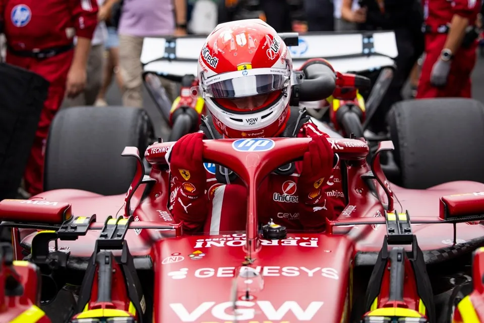 Un pilot de Formula 1 cu cască roșie și albă stă în cockpitul unei mașini de curse de culoare roșie.