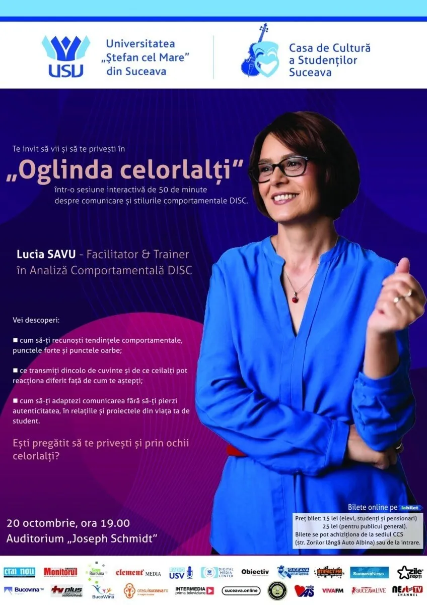 O femeie cu ochelari și bluză albastră stă în fața unui fundal violet pe care sunt scrise diverse texte și simboluri grafice.