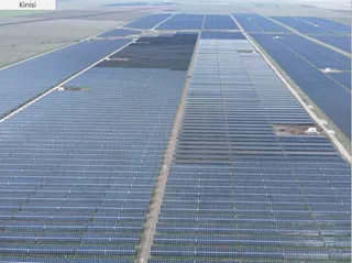 Vedere aeriană cu rânduri paralele de panouri fotovoltaice albastre, despărțite de poteci înguste și zone de pământ.