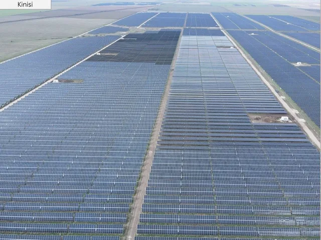 Vedere aeriană cu rânduri paralele de panouri fotovoltaice albastre, despărțite de poteci înguste și zone de pământ.