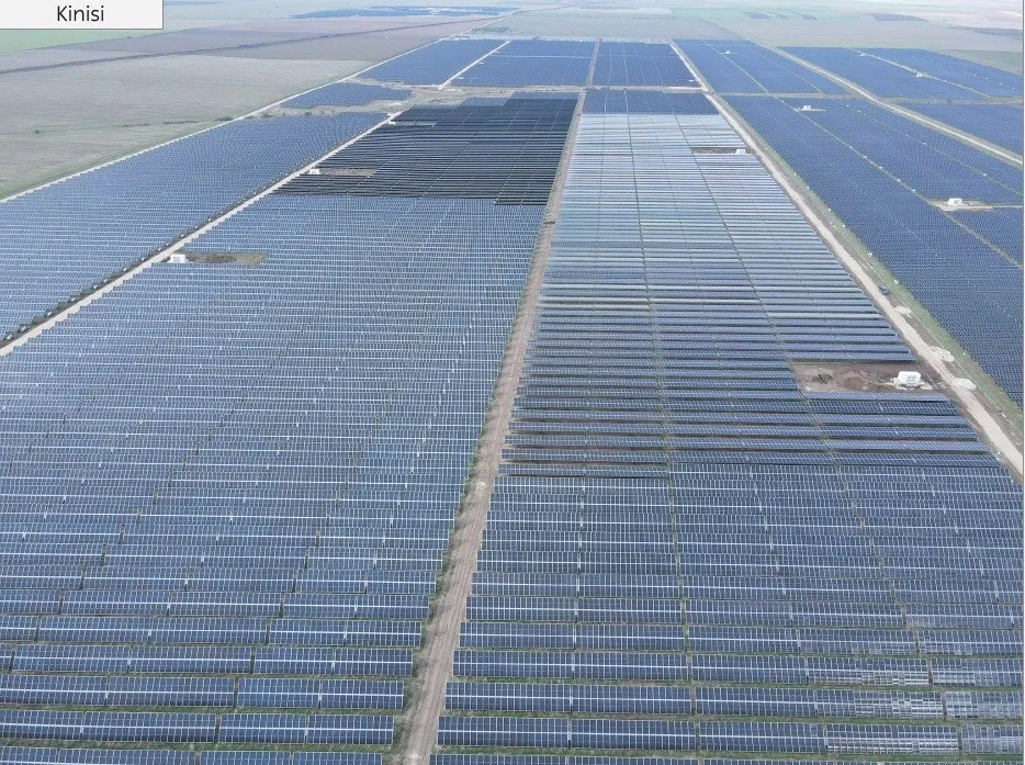 Vedere aeriană cu rânduri paralele de panouri fotovoltaice albastre, despărțite de poteci înguste și zone de pământ.