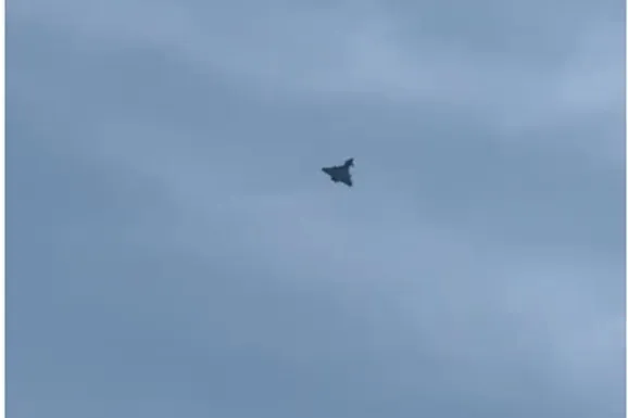Un avion de vânătoare zboară pe un cer acoperit de nori gri.
