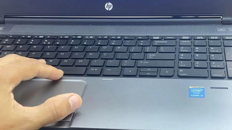 O mână folosește touchpad-ul unui laptop negru de lângă tastatura cu taste de tip qwerty.