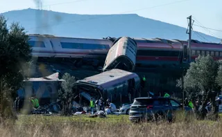 Vagoane de tren de culoare albă și roșie sunt răsturnate pe un câmp lângă vegetație, în prezența unor persoane și vehicule.