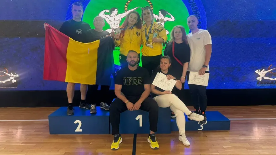 Un grup de șapte persoane posedă o medalie, un trofeu și un steag, stând pe un podium de premiere în fața unui ecran albastru.