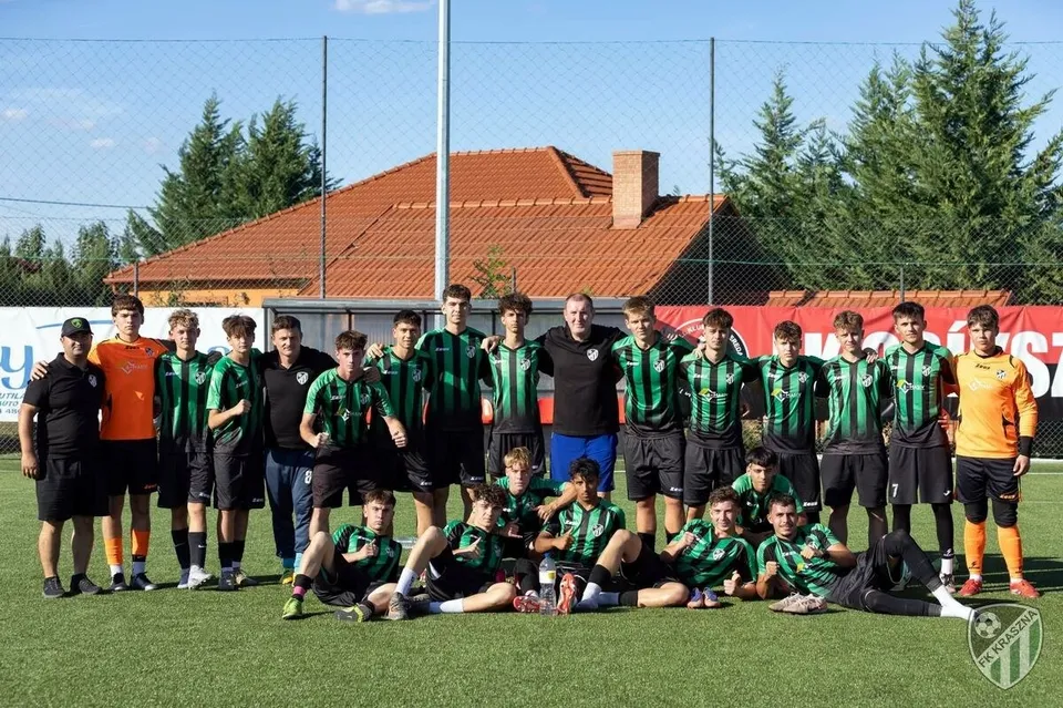 Un grup de tineri sportivi în echipamente verzi și negre pozează pe un teren de fotbal verde sub un cer senin.