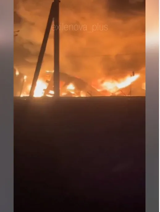 Flăcări mari și fum se ridică deasupra unor structuri metalice sub un cer nocturn portocaliu.