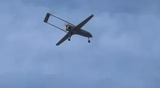 O dronă cu două aripi lungi și un cadru de susținere în spate zboară pe un cer înnegurat de nori.