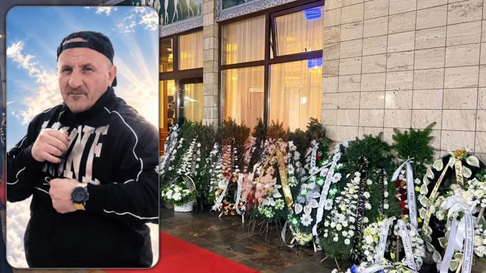 Un bărbat cu șapcă neagră și hanorac negru este suprapus pe o imagine cu numeroase coroane de flori așezate în fața unei clădiri.