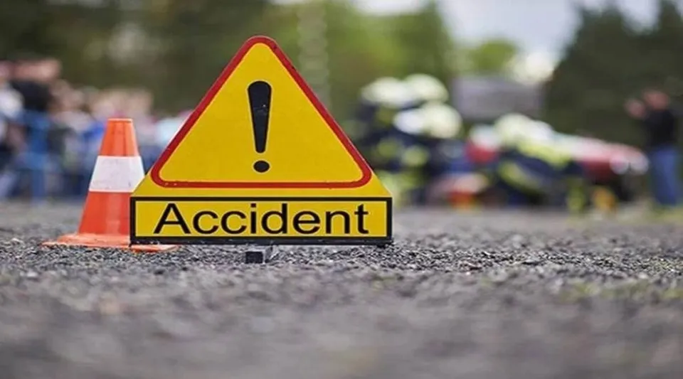 Un semn de avertizare triunghiular galben cu un punct exclamării și cuvântul Accident este plasat pe un drum lângă un con portocaliu.