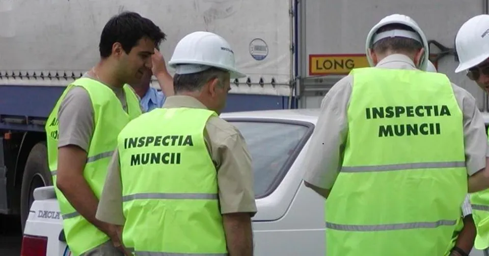 Patru bărbați poartă veste reflectorizante galben-verzui, dintre acestea două având inscripția Inspectia Muncii, stând lângă un vehicul alb.