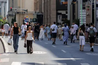 Oamenii merg pe o stradă asfaltată cu clădiri și semne de circulație în fundal.