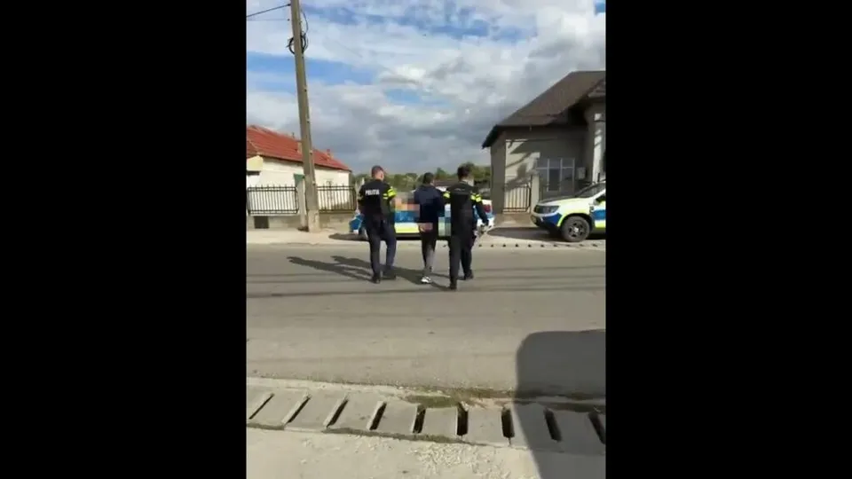 Trei persoane în uniforme de culoare închisă cu elemente galben fluorescente stau pe un drum lângă un autoturism alb și un vehicul de poliție.