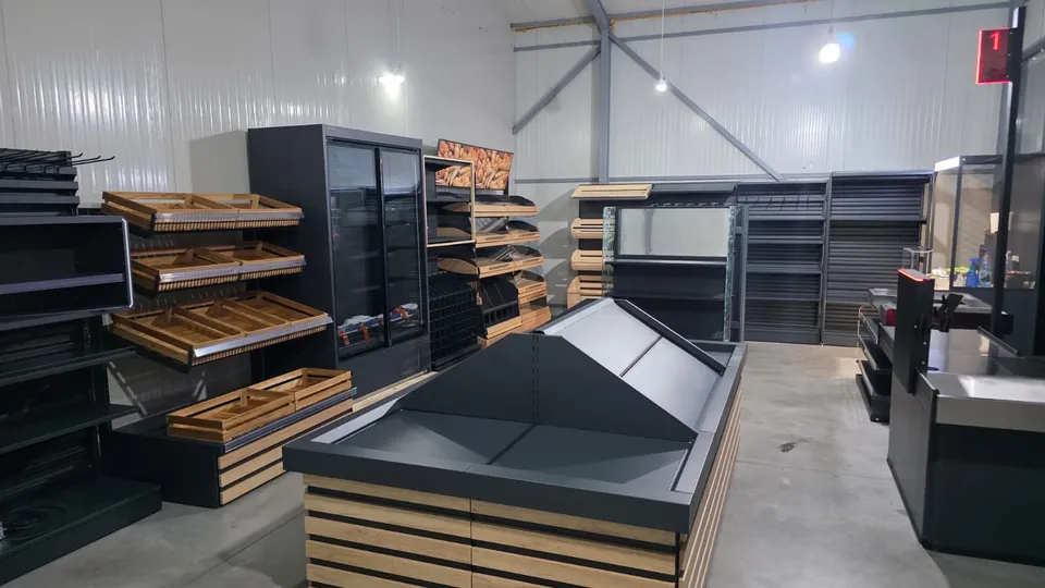 Mobilier comercial de culoare închisă și rafturi din lemn sunt dispuse într-un spațiu de depozitare sau showroom cu pereți metalici albi.
