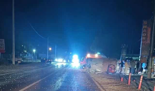 Două vehicule și un vehicul de serviciu sunt parcate pe marginea unui drum asfaltat noaptea, sub lumini strălucitoare.