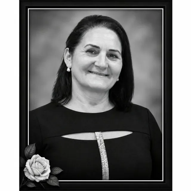 O femeie zâmbindă cu părul negru și haine negre este prezentată într-o fotografie de tip portret încadrată, lângă o petală de trandafir în colțul din stânga jos.