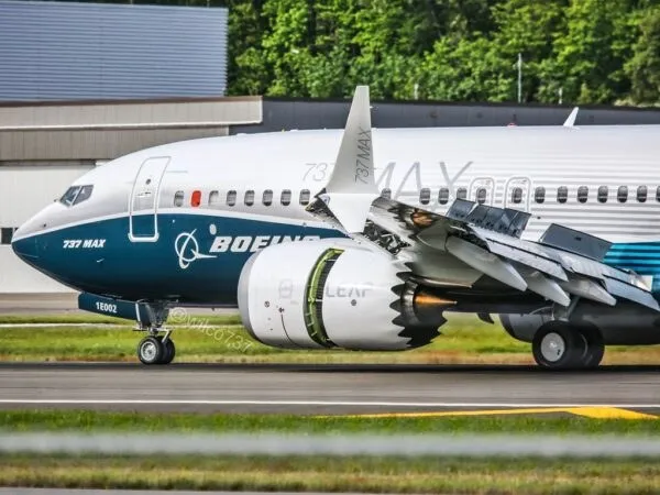 Un avion alb cu inscripția Boeing 737 MAX este parcat pe o pistă de aterizare lângă o zonă cu vegetație verde.