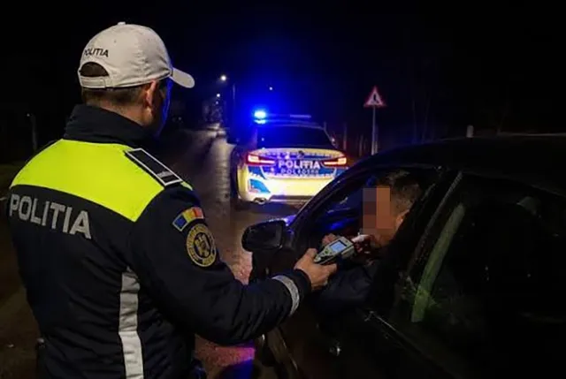 Un polițist în uniformă cu vestă reflectorizantă folosește un aparat de testare lângă fereastra deschisă a unui autoturism noaptea.
