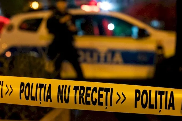 O bandă galbenă cu textul scris în negru este întinsă în prim-plan, în fața unei mașini de poliție și a unei siluete întunecate.