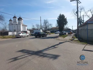 O stradă asfaltată cu mașini parate pe margini, o clădire albă cu turnuri și un stâlp de utilități sub un cer senin.