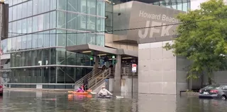O clădire modernă cu inscriptionatul 'Howard Beach JFK' este înconjurată de ape inundate, în timp ce persoane în canoe navighează prin apă lângă scară.