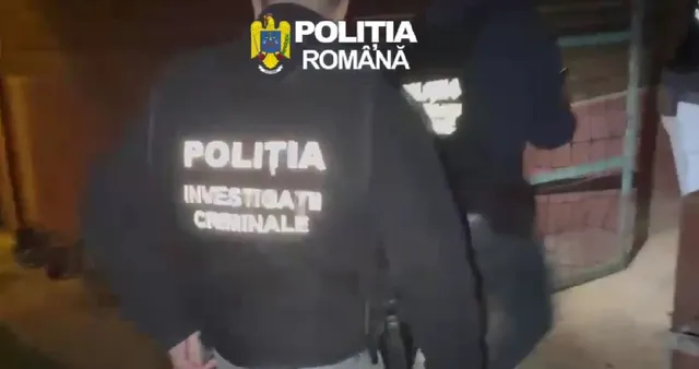 Un membru al poliției poartă un hanorac negru pe care scrie textul alb "POLIȚIA INVESTIGAȚII CRIMINALE".