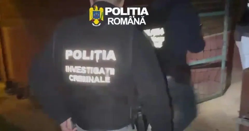Un membru al poliției poartă un hanorac negru pe care scrie textul alb "POLIȚIA INVESTIGAȚII CRIMINALE".