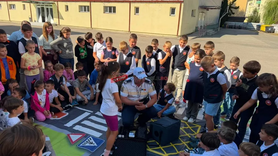 Un grup de copii stă pe un desen de drum marcat pe asfalt, în timp ce un bărbat în uniformă le vorbește.