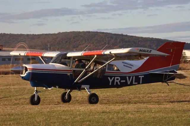 Un avion mic cu elice, de culoare albastră și albă, stă pe o pistă de iarbă sub un cer înnorat.