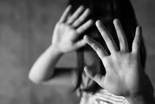 O persoană cu părul lung ridică ambele mâini cu palmele spre înainte într-o poziție de oprire, într-o imagine alb-negru.
