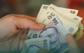 Două mâini țin un teanc de bancnote de 50 și 100 de lei.