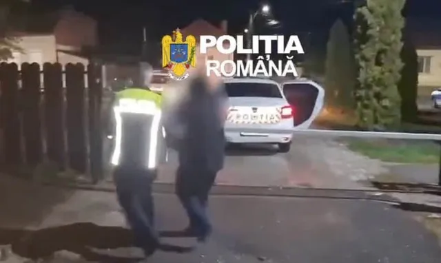 Un agent de poliție în uniformă reflectorizantă stă lângă un vehicul alb cu portierea deschisă pe un drum de noapte.