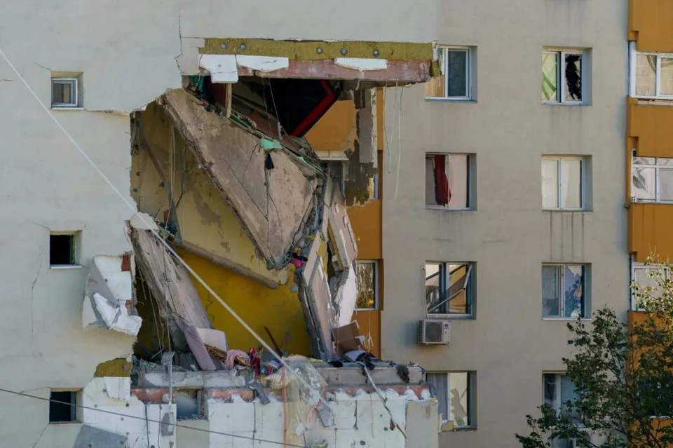 O secțiune de fațadă a unei clădiri de apartamente este lipsită, expunând structura interioară și resturi de beton și materiale de construcție.
