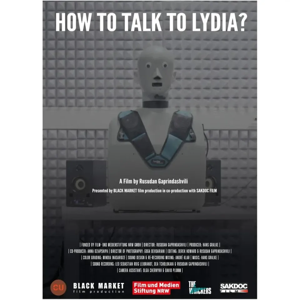 Un poster afișează un robot cu cap alb și corp gri în fața unui perete cu textură pătrată.
