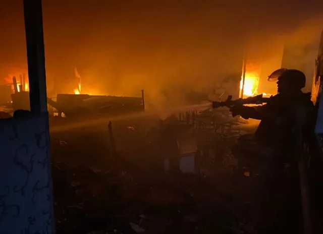 Silueta unui soldat cu o armă este vizibilă în prim-plan, în fața unui incendiu intens care luminează un teren de noapte.