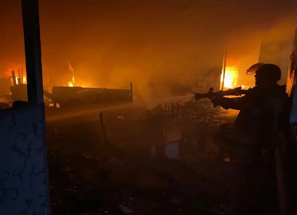 Silueta unui soldat cu o armă este vizibilă în prim-plan, în fața unui incendiu intens care luminează un teren de noapte.