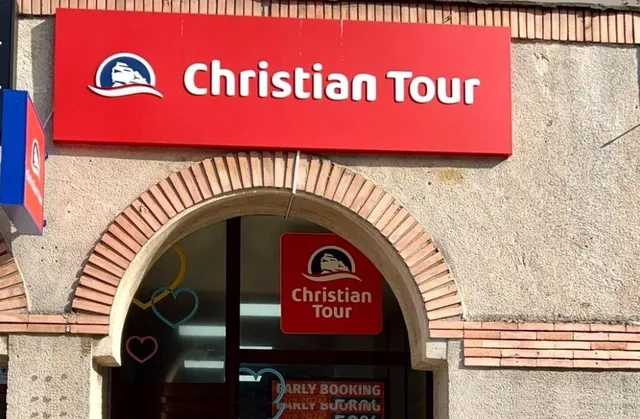 Un panou roșu cu textul alb și un logo reprezintă agenția Christian Tour pe fațada unei clădiri.
