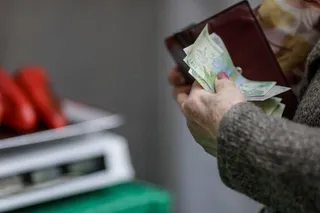 Mâinile unei persoane țin un portofel deschis din care ies câteva bancnote de culoare verde.