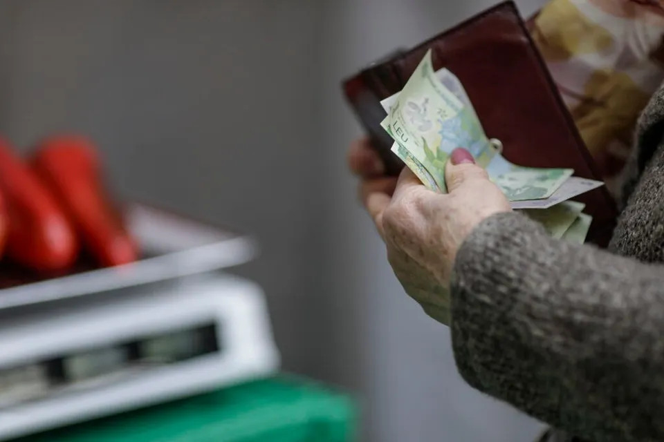 Mâinile unei persoane țințin un portofel deschis din care ies câteva bancnote de culoare verde.