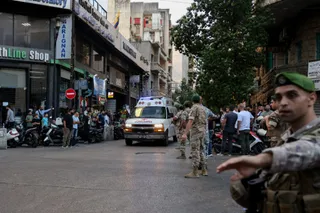Un grup de bărbați în uniforme militare stă pe un drum urban lângă o ambulanță albă și vehicule parcate.