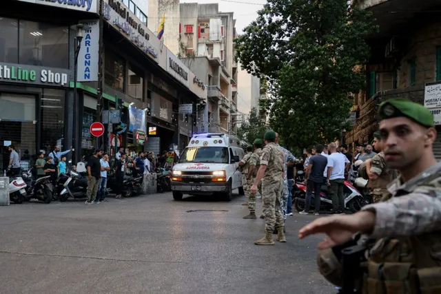 Un grup de bărbați în uniforme militare stă pe un drum urban lângă o ambulanță albă și vehicule parcate.