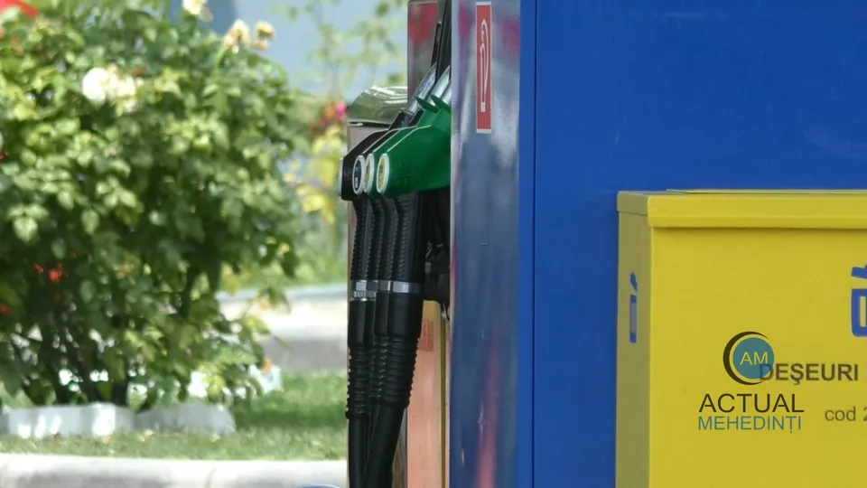 Două duze de pompat combustibil negre cu accesorii verzi sunt suspendate pe o stație de alimentare lângă un recipient galben.