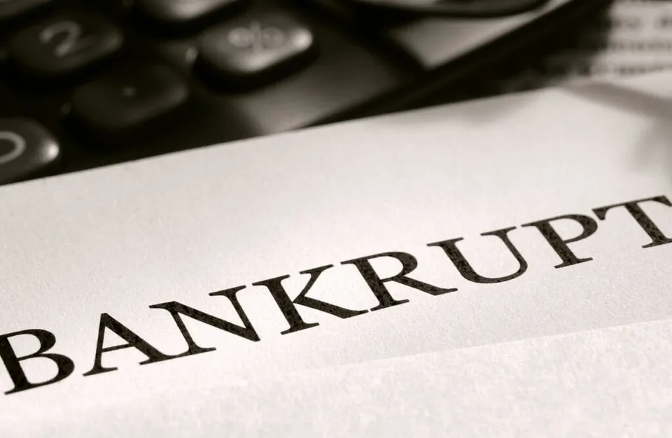 Cuvântul BANKRUPT este imprimat pe o foaie de hârtie lângă un calculator de masă.