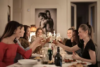 Un grup de femei stă la o masă din interior și ridică pahare de sticlă pentru un toast.